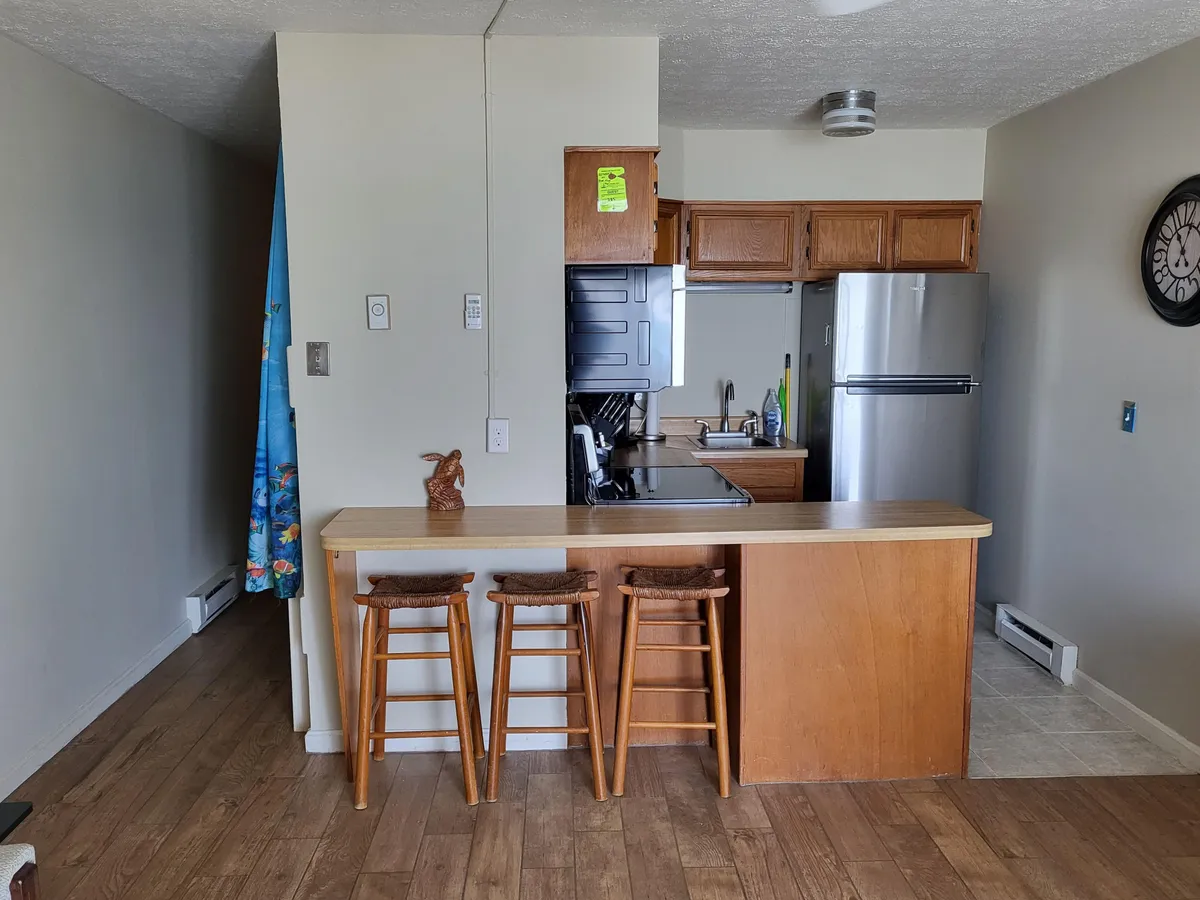 An inviting kitchen island with stools, appliances, and curtains filtering natural light. The setup encourages socializing or enjoying a meal, with ample counter space and a casual, friendly vibe.