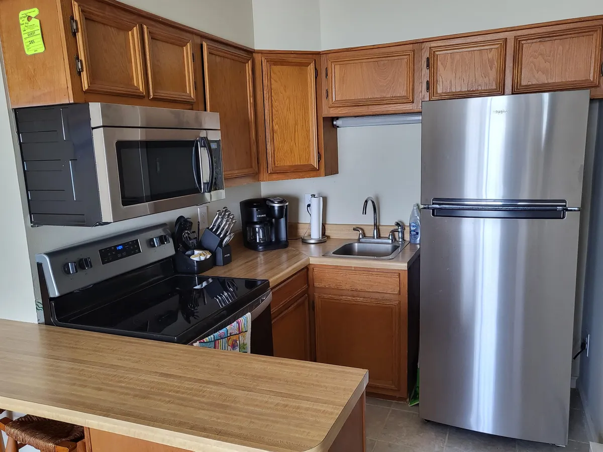 A practical and well-equipped kitchen featuring stainless steel appliances, a black stove and microwave, wooden cabinets, and countertop appliances. The setup is ideal for cooking meals or entertaining guests, exuding a sense of comfort and convenience.