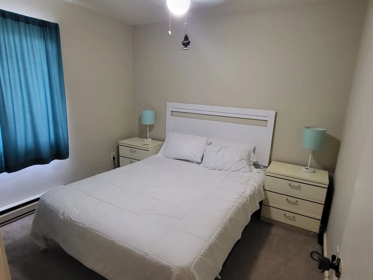 A tranquil bedroom scene featuring a cozy bed with crisp linens, flanked by matching nightstands and softly illuminated by natural light streaming through the window. The overall atmosphere is calm and welcoming, inviting restful sleep and relaxation.