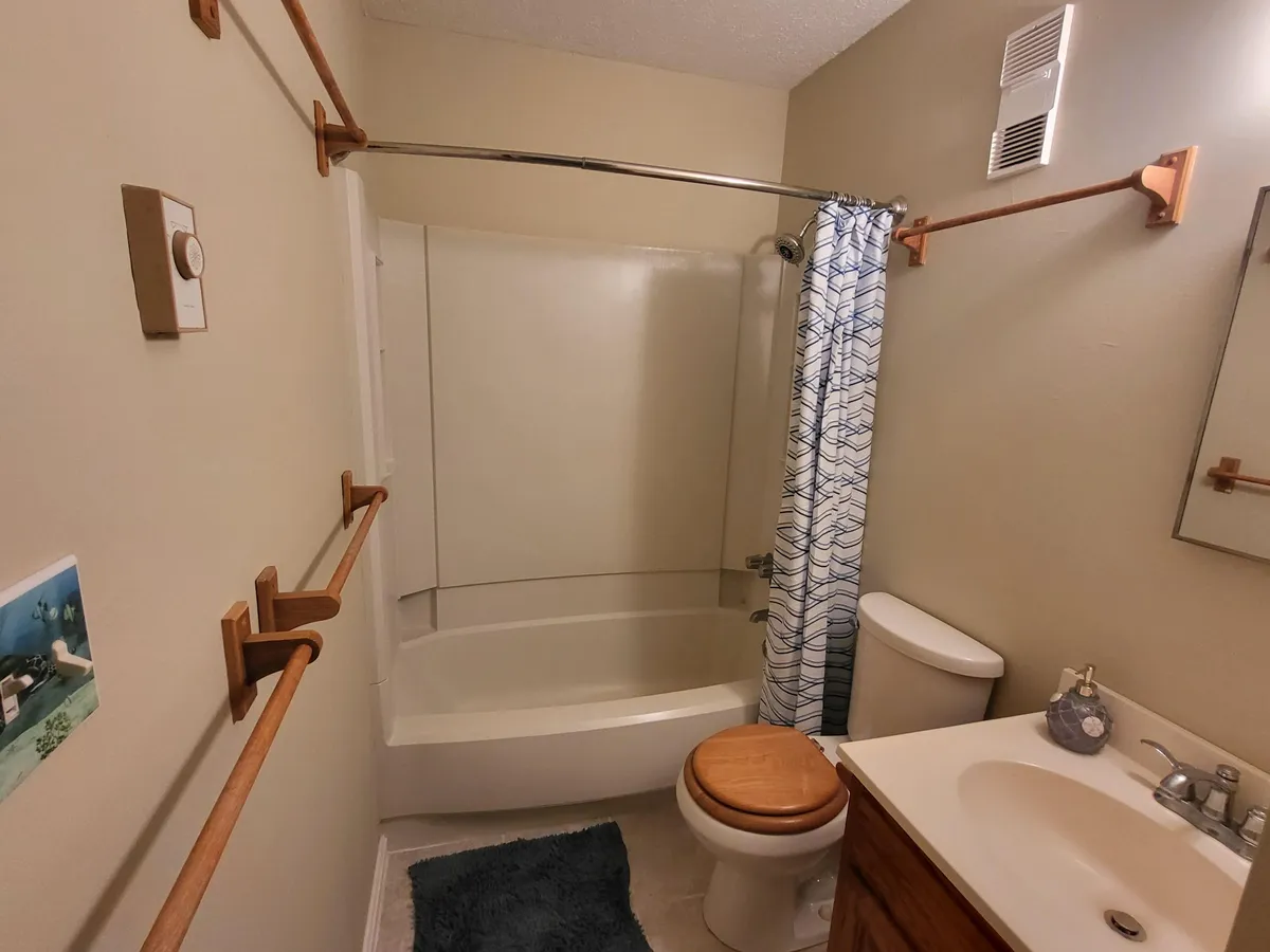 A modern and clean private bathroom featuring a bathtub, shower, sink, and toilet, framed by practical wooden towel racks and a calming color palette. The space feels both functional and relaxing, supporting moments of self-care.