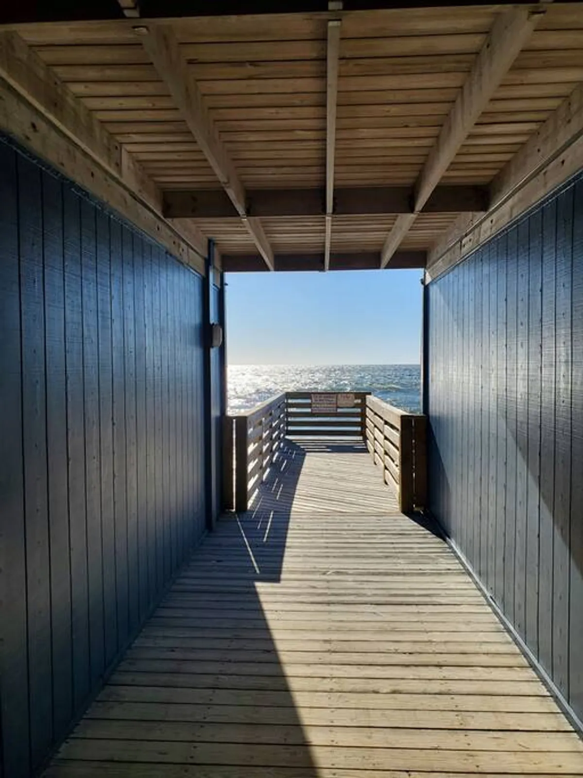 A serene exterior shot featuring a wooden walkway leading towards an expansive ocean view. The sky is calm, and the scene evokes a sense of peace and escape, ideal for leisurely strolls or peaceful contemplation by the water.
