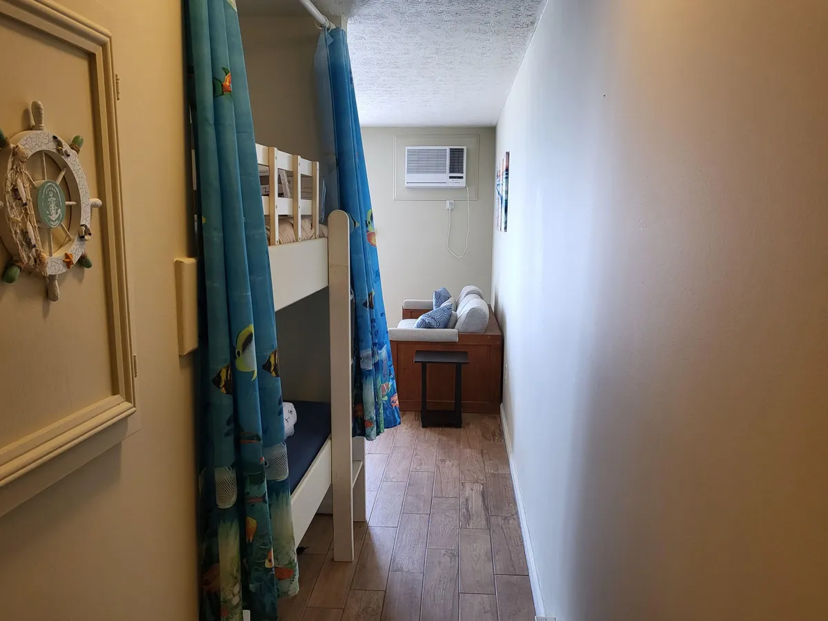 A playful and welcoming bedroom with a colorful bunk bed, small seating area, and decorative beach-themed wall art. The space feels family-friendly and designed for relaxation, echoing the condo's inviting atmosphere.