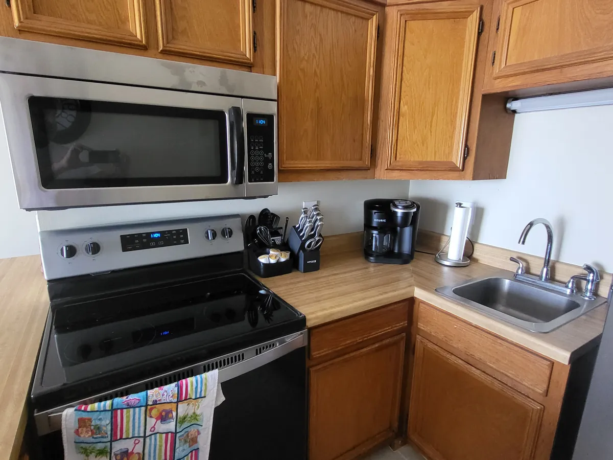 A cozy, functional kitchen featuring stainless steel appliances, wooden cabinetry, and a sparkling countertop with a colorful dish towel. The layout invites both meal preparation and social interaction, with practical touches like a coffeemaker visible.